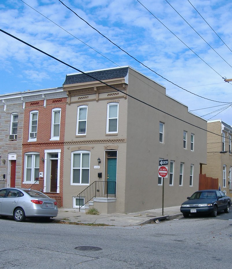 1224 W. Ostend Street after renovation. Baltimore city corner rowhome with beige painted brick and a blue front door.