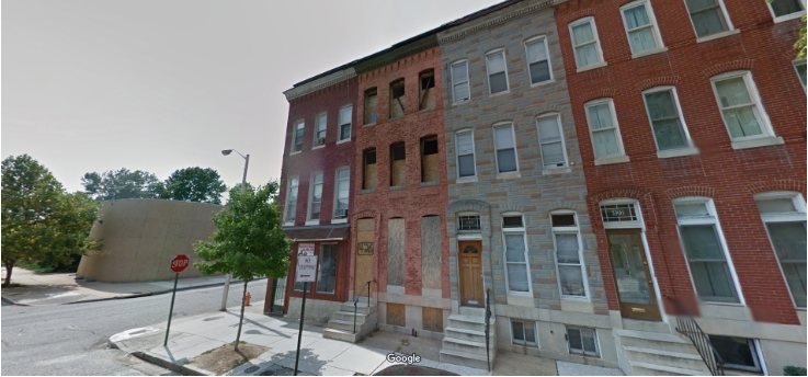 426 Mosher Street exterior before renovation. Red brick shell townhome in Baltimore City with boarded doors and windows.