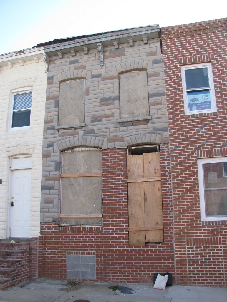 1121 Ward Street before renovation. Baltimore City rowhome with boarded windows and doors. Half formstone, half brick walls.