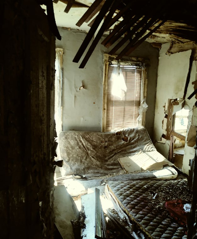 2125 Denison Street interior before renovation. Wood shards and broken windows. Distressed mattresses on the floor. 
