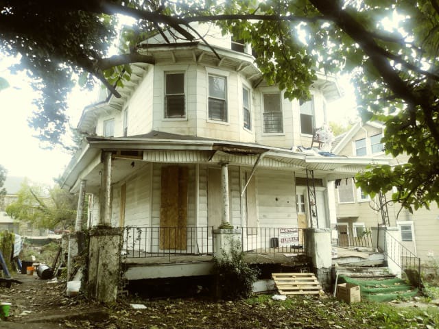2125 Denison Street before renovation. Four unit home with boarded doors and littered yard.