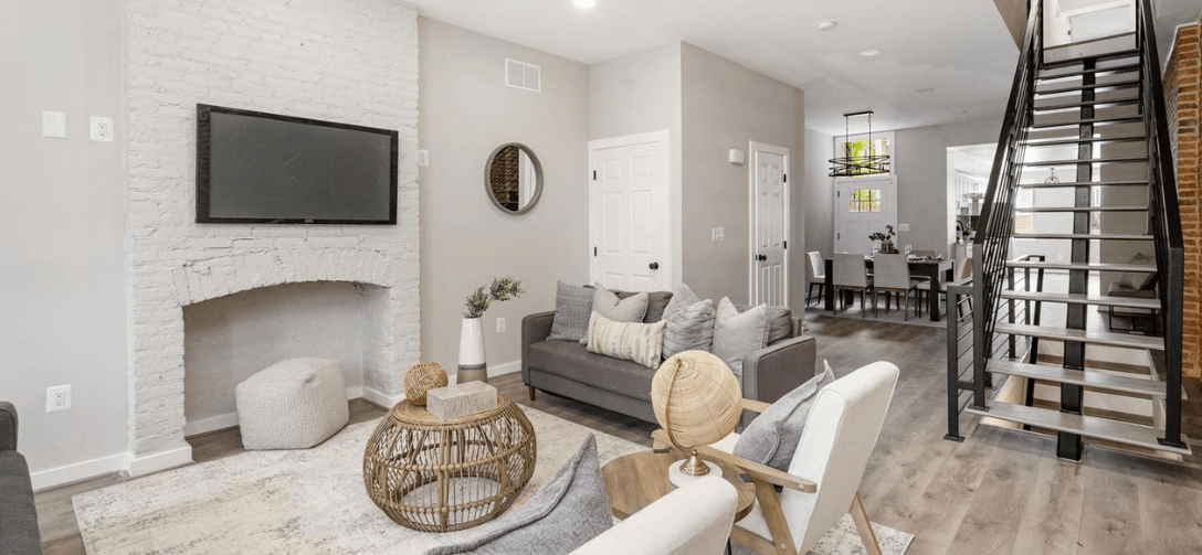824 Edmondson Avenue interior after renovation. Exposed brick wall with display niche, gray furniture, bright natural lighting coming though window near white door.